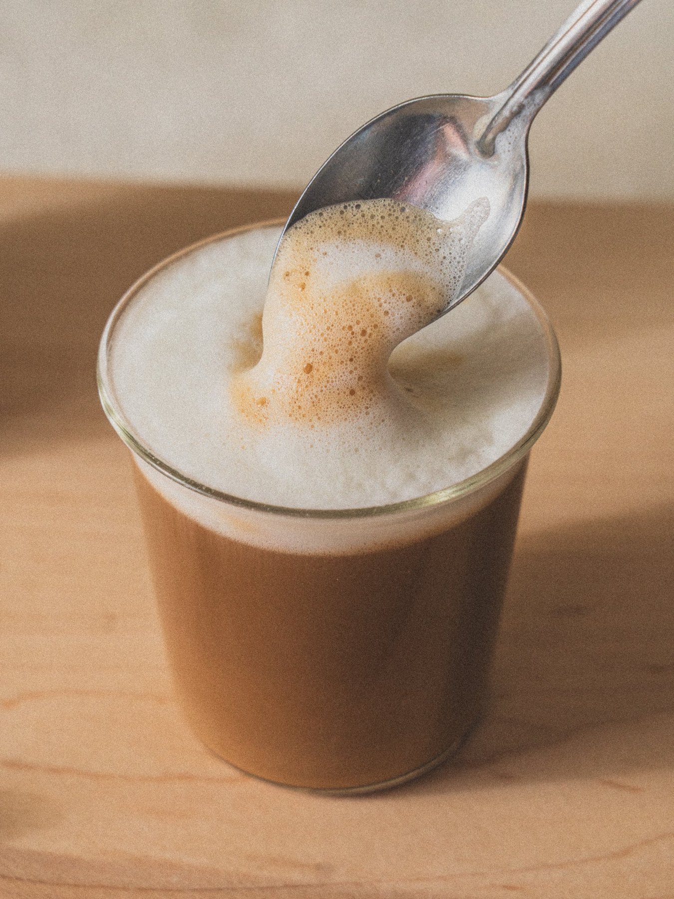 Frothed beverage in glass cup on wooden surface with spoon.