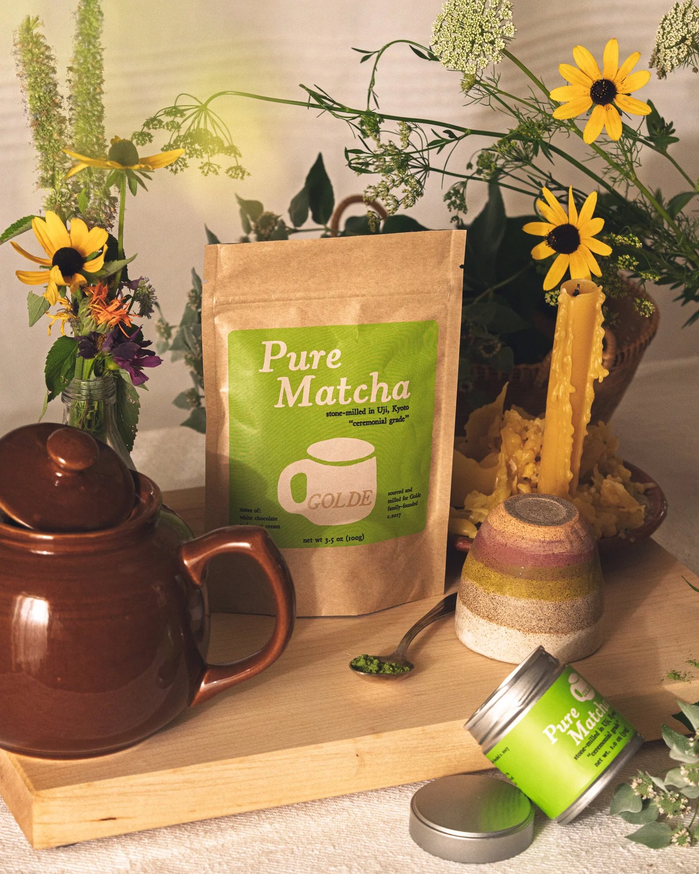 Tabletop still life featuring matcha sachets teapot and fresh flowers.