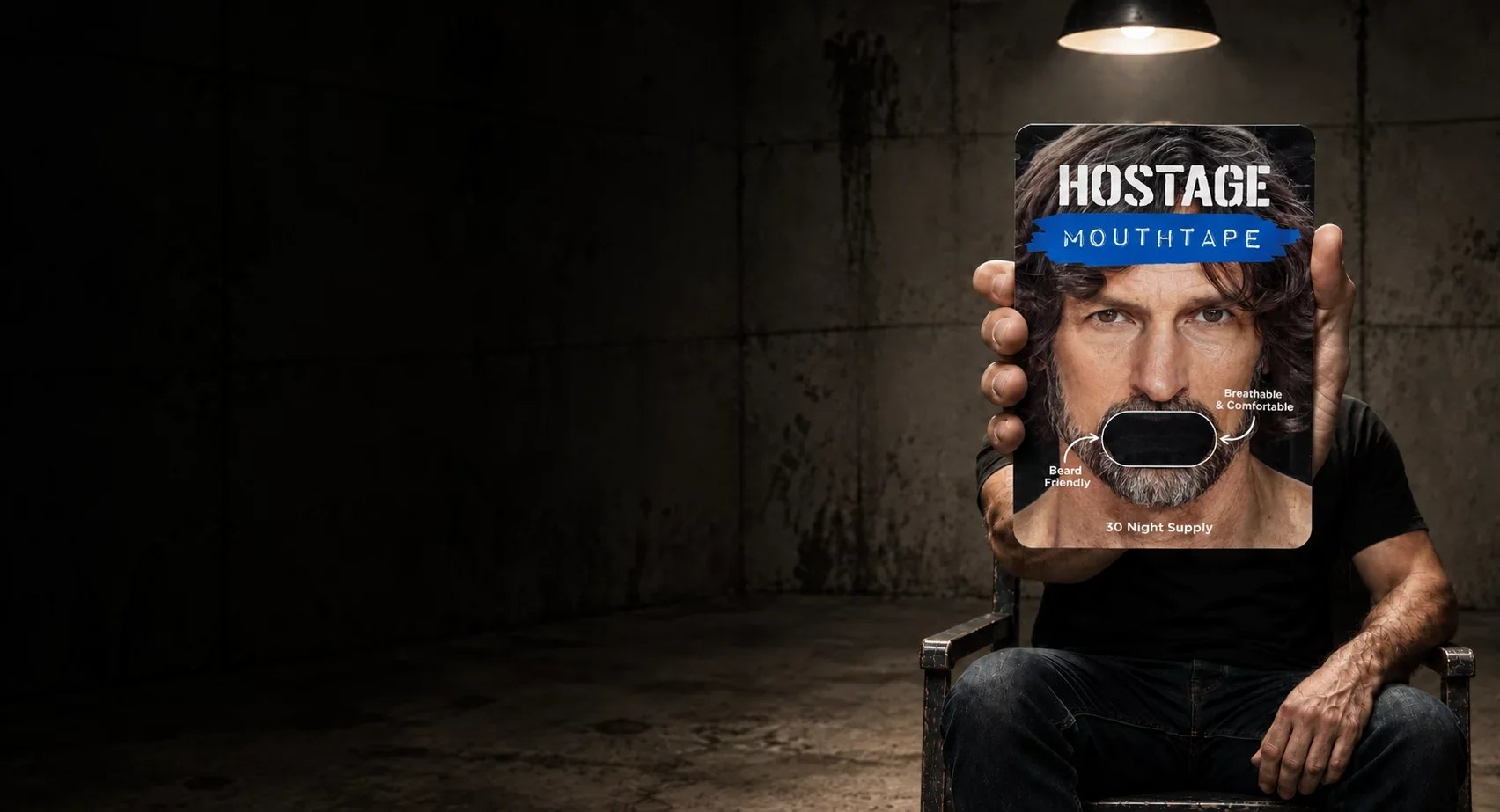 Seated man holding Hostage Mouth Tape pack forward.
